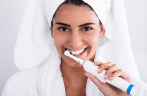 Beautiful Woman In Bathrobe Brushing Teeth Using Electric Toothbrush