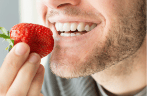 Young man holding a strawberry and smiling