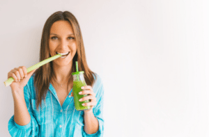 woman with stick of green organic celery and fresh homemade celery juice.