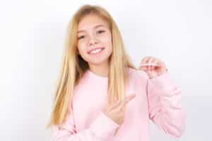 little girl wearing pink sweater over white background holding an invisible aligner 300x200 1