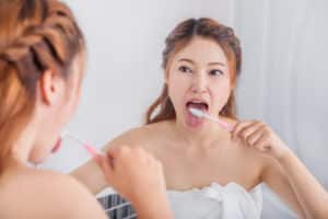 woman cleaning tongue using toothbrush with mirror in the bathroom