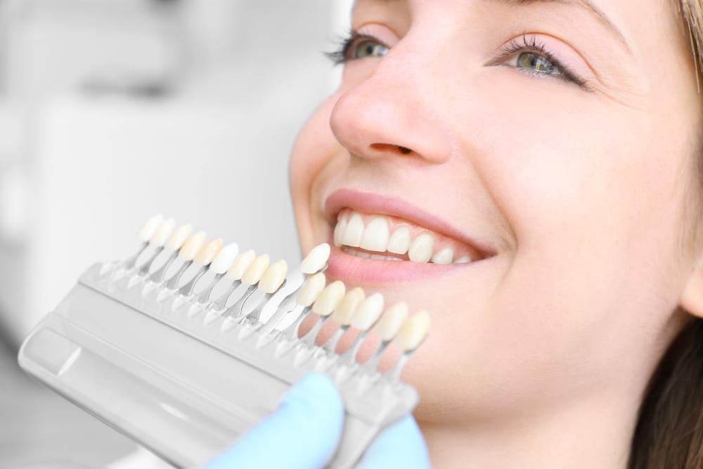 Young woman at dentist office checking and selecting colour of the teeth