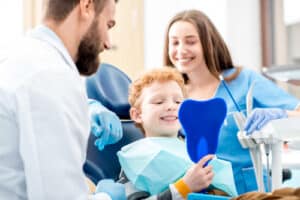 Young boy looking at the mirror with toothy smile sitting on the chair with dentist