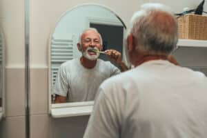 Elderly man brushing his teeth to maintain his oral health as he ages.