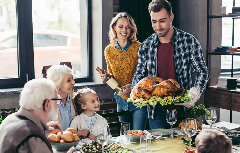 Man holding Thanksgiving turkey with family at the dinner table