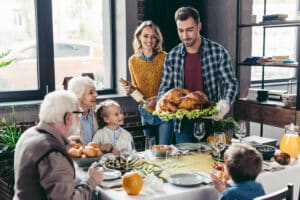Man holding Thanksgiving turkey with family at the dinner table