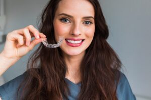 Young woman smiling with straight teeth and holding clear aligners