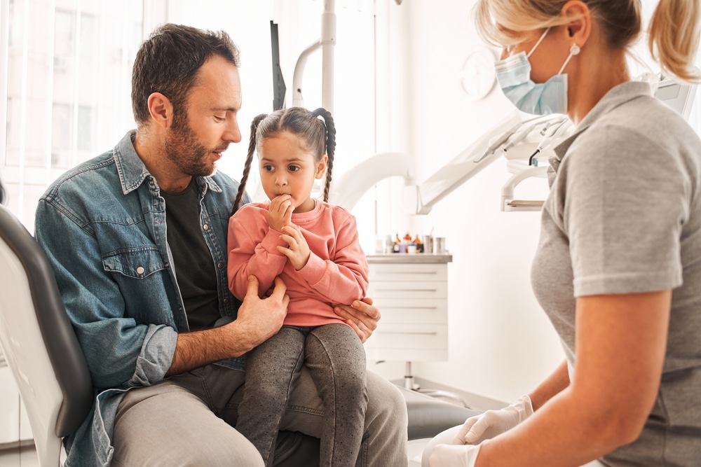 Dad holding daughter talking to dentist during family dental appointment.