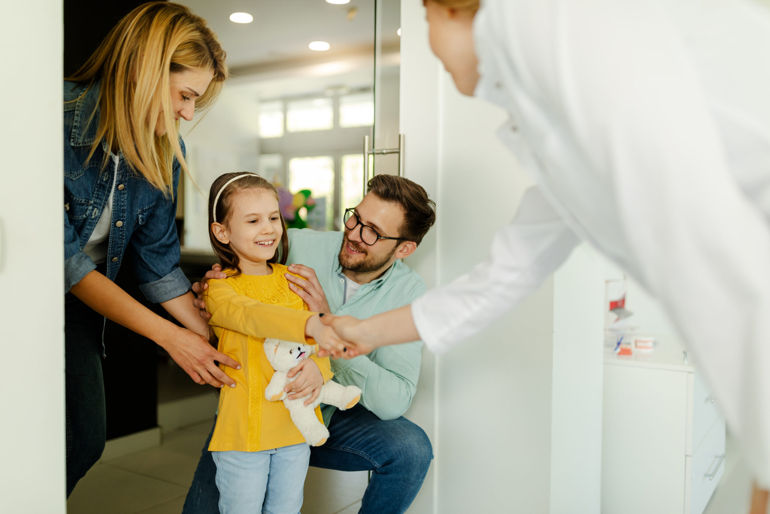 Dentist shaking little girl's hand while her parents smiling and encouraging her