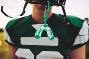 Close-up of a football player with a mouthguard hanging from his helmet faceguard, emphasizing sports dental protection