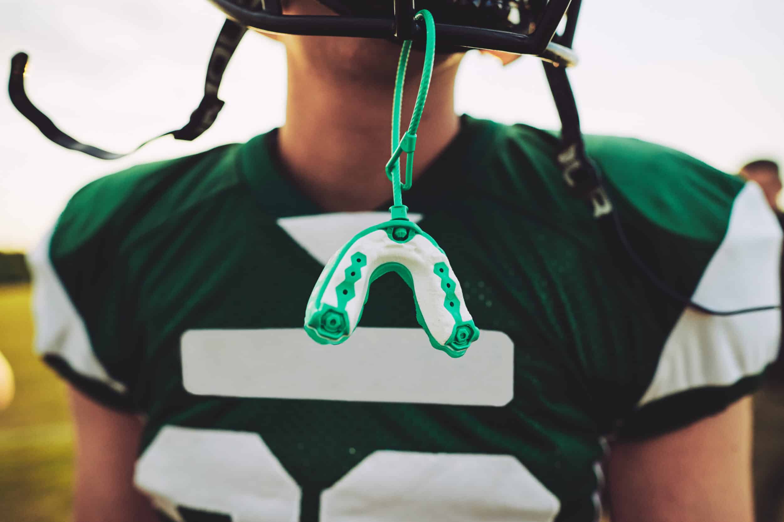 Close-up of a football player with a mouthguard hanging from his helmet faceguard, emphasizing sports dental protection