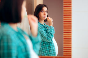 Pregnancy woman looking in the mirror while she brushes her teeth